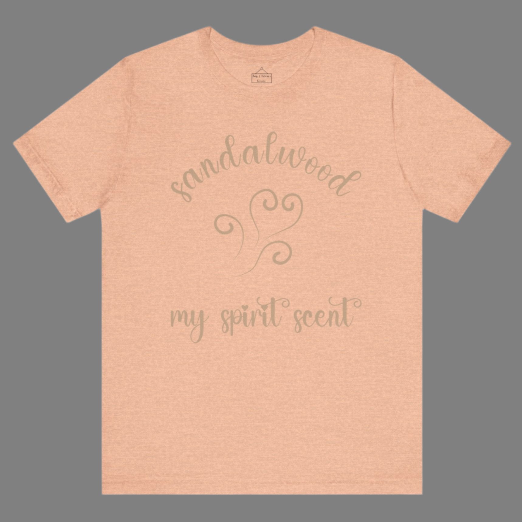 The My Spirit Scent is Sandalwood t-shirt in heather peach featuring script font and an aroma script heart in a warm, muted beige hue