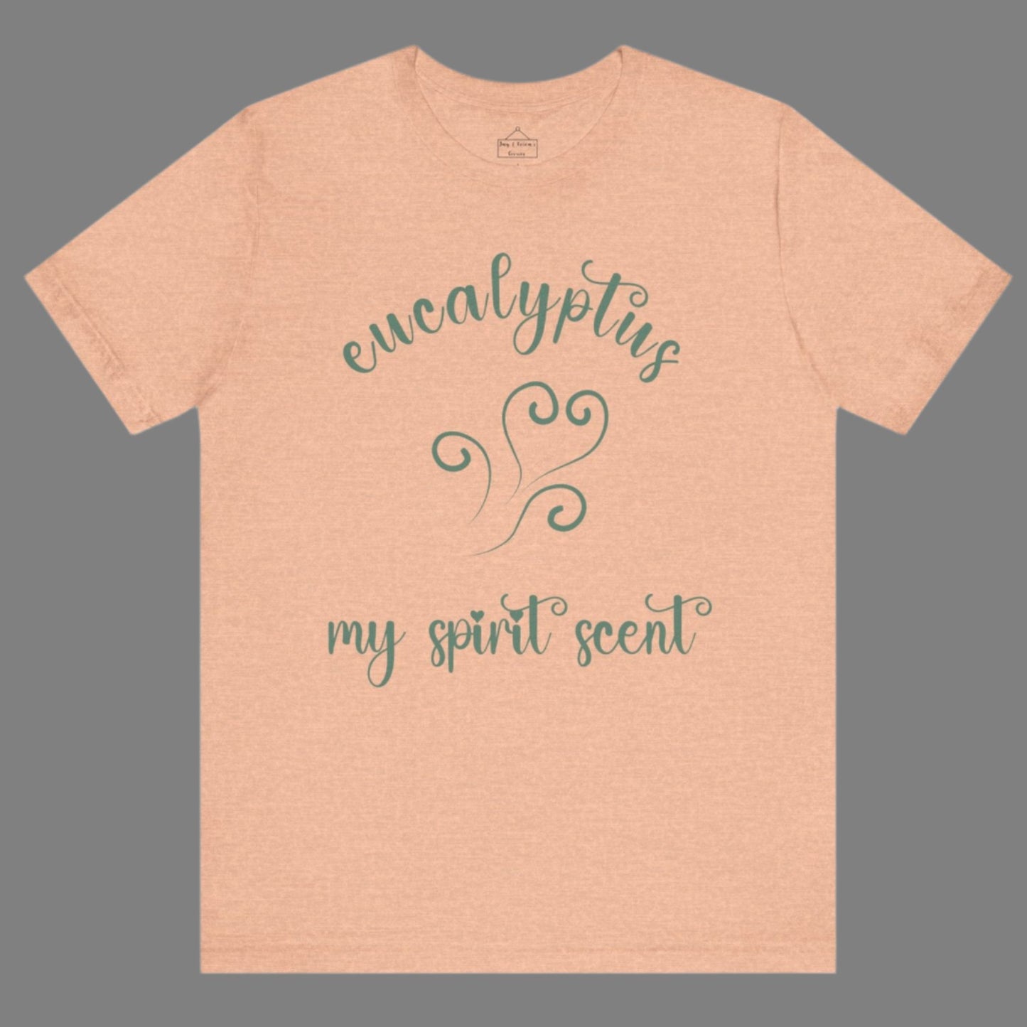 The My Spirit Scent is Eucalyptus t-shirt in heather peach featuring script font and an aroma script heart in a blue-green hue