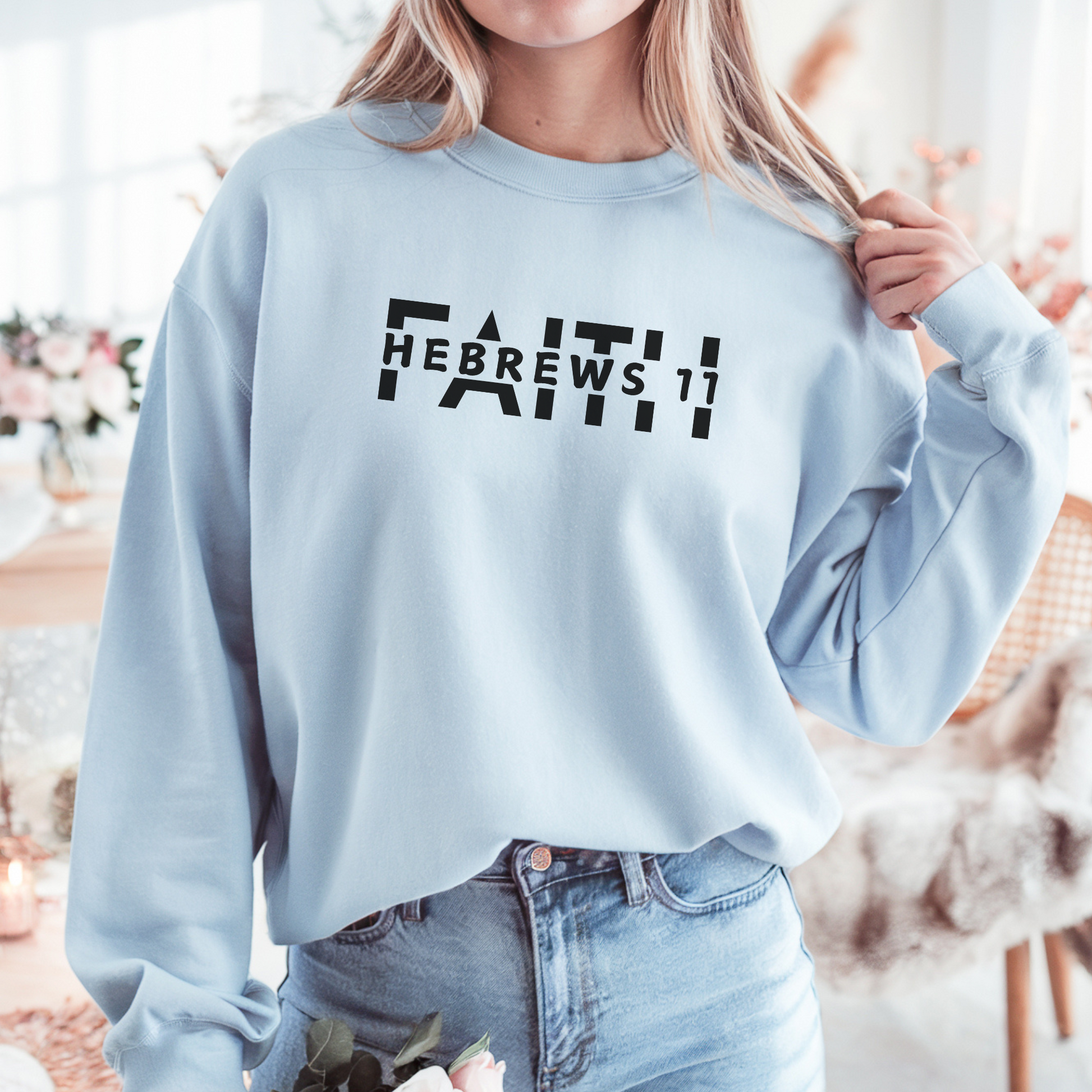 A smiling woman wearing the FAITH Hebrews 11 sweatshirt in light blue featuring the word faith with Hebrews 11 cut between the letters all in black print