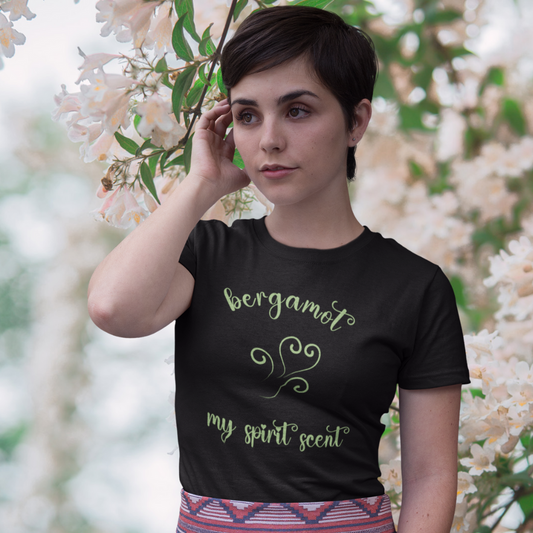 A woman standing rather curiously in front of a cherry blossom backdrop wearing the My Spirit Scent is Bergamot t-shirt in black with script font and an aroma script heart both in a lively green hue