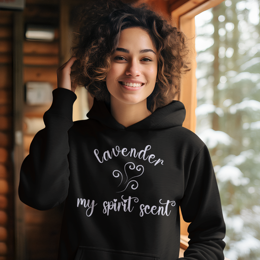 A smiling woman in a cozy winter cabin wearing the My Spirit Scent is Lavender hoodie in black with script font and an aroma script heart both in a soft lavender hue