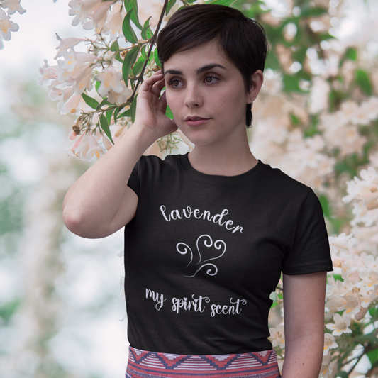 A woman standing rather curiously in front of a cherry blossom backdrop wearing the My Spirit Scent is Lavender t-shirt in black heather with script font and an aroma script heart both in a soft lavender hue