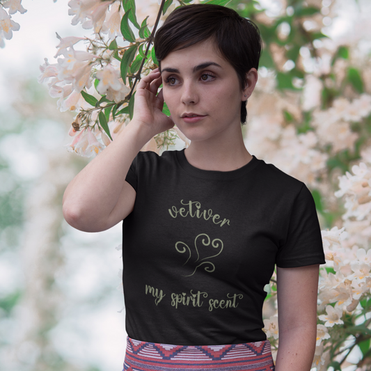 A woman standing rather curiously in front of a cherry blossom backdrop wearing the My Spirit Scent is Vetiver t-shirt in black heather with script font and an aroma script heart both in a grey-green hue