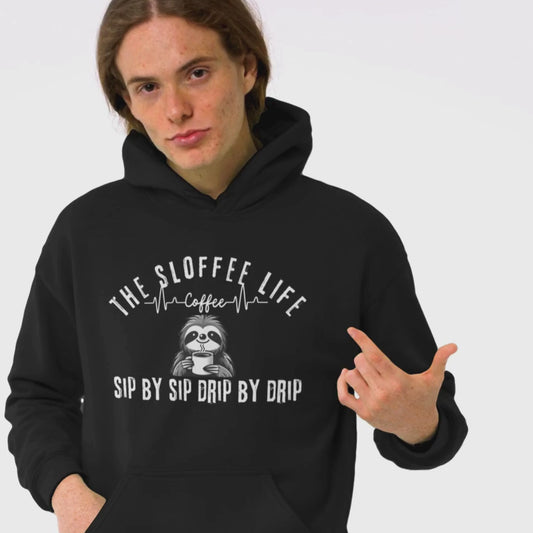 Happy young man in a studio setting wearing The Sloffee Life Espresso Yourself Slowly hoodie in black featuring a sloth drinking coffee
